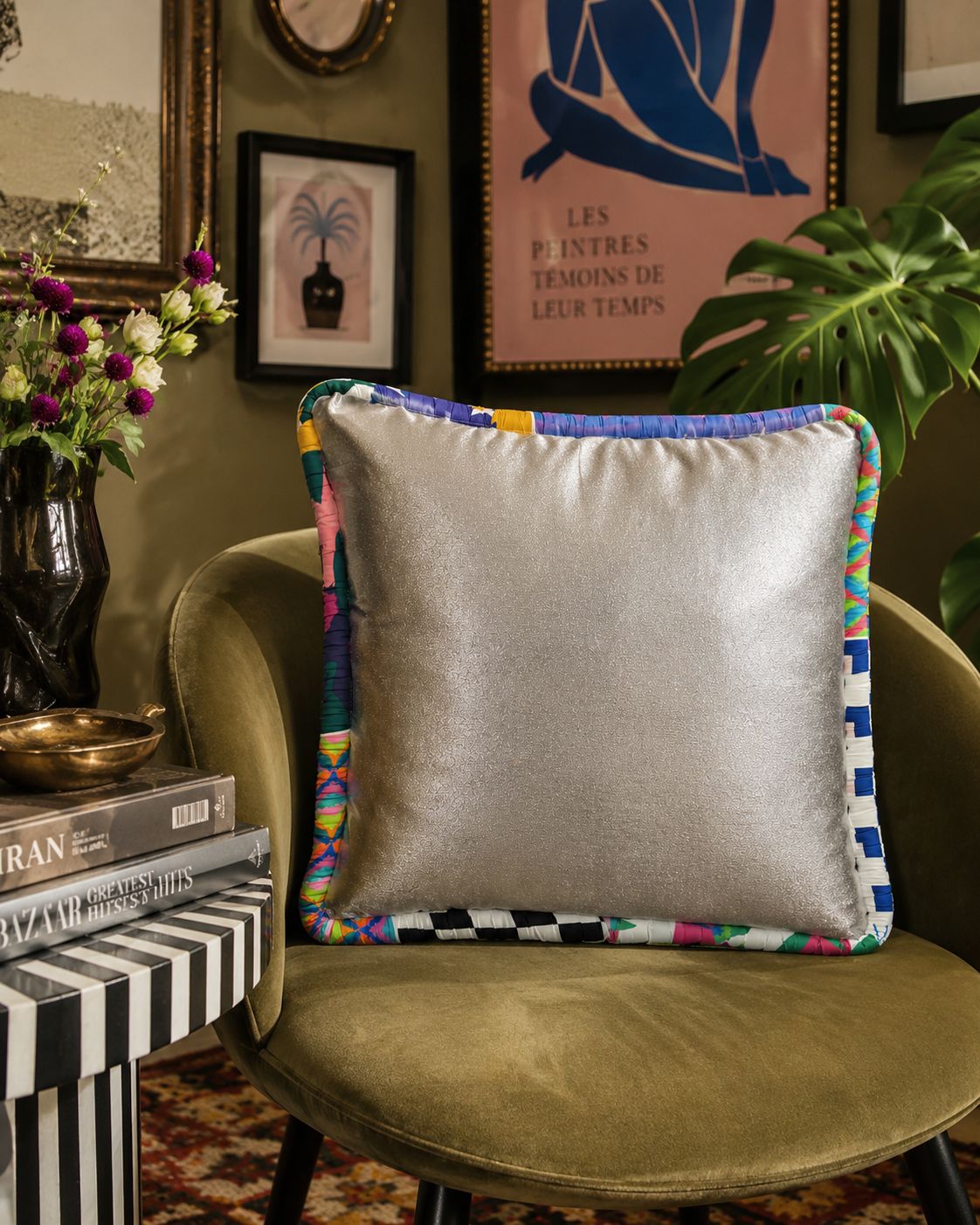 Decorative pillow with colorful trim on a green chair in a room with art and plants.