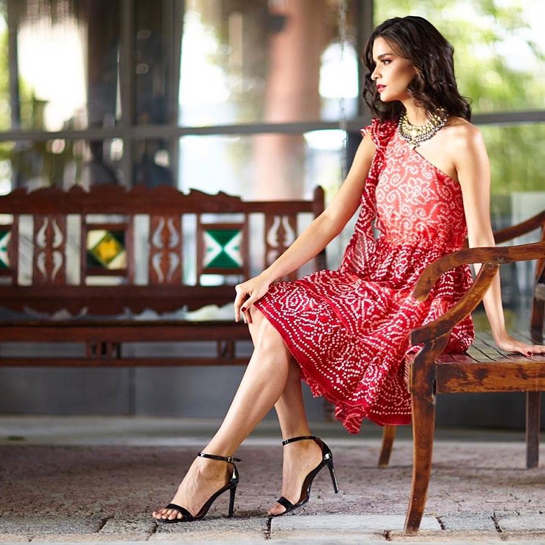 Woman in a red patterned dress sitting on a wooden bench outdoors.