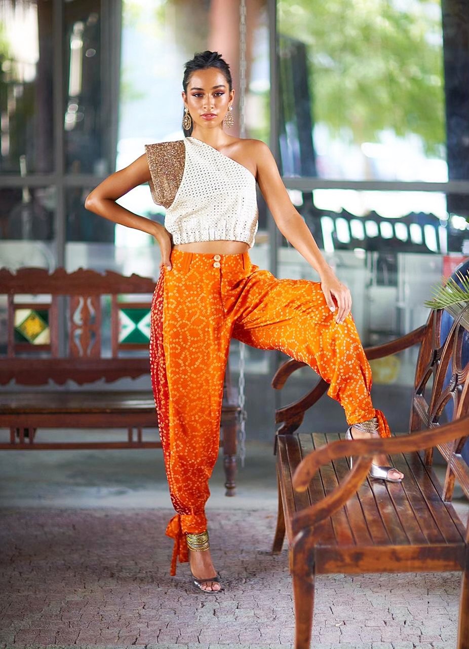 Woman in a white top and orange pants posing outdoors.