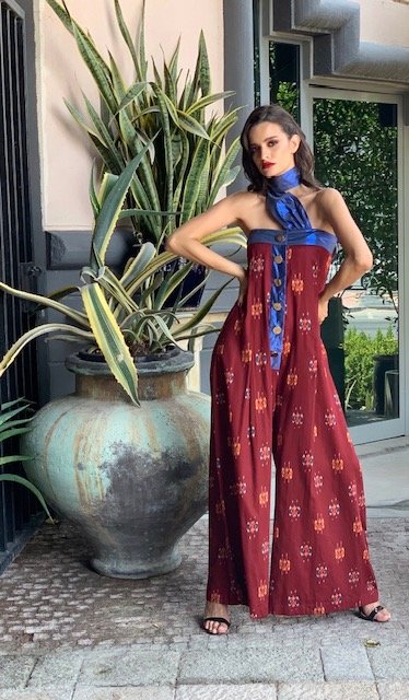 Woman in a red patterned dress with a blue scarf standing next to a large potted plant.