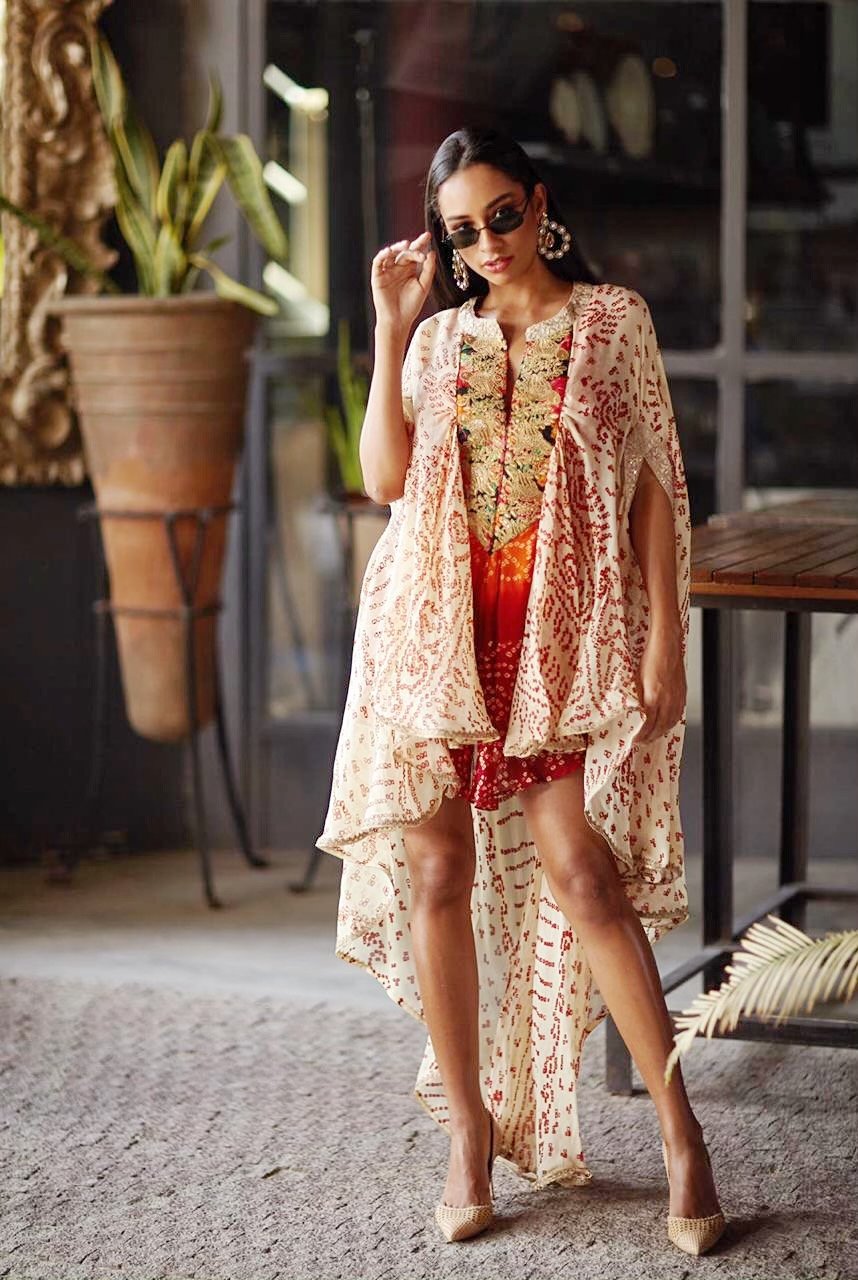 Woman in a floral kimono-style garment standing in an indoor setting with plants and furniture.