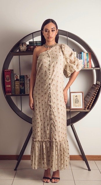 Woman in a beige patterned dress standing in front of a round mirror with books on a shelf.