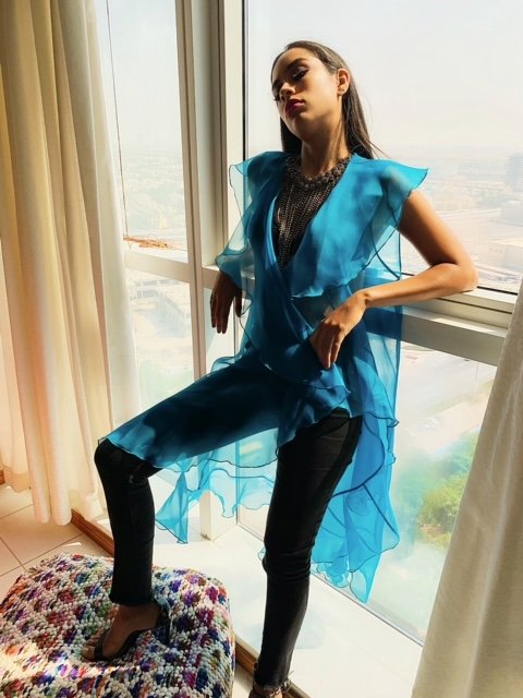 Woman wearing a blue outfit with ruffled sleeves in a bright room.