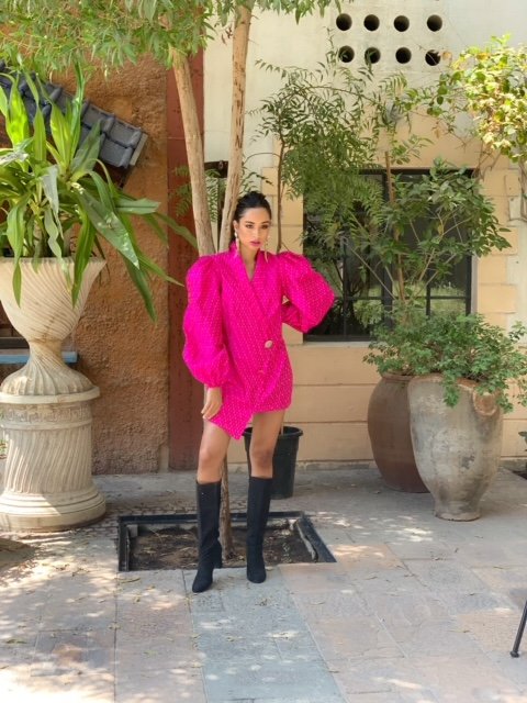 Person wearing a bright pink dress with black knee-high boots standing outdoors.
