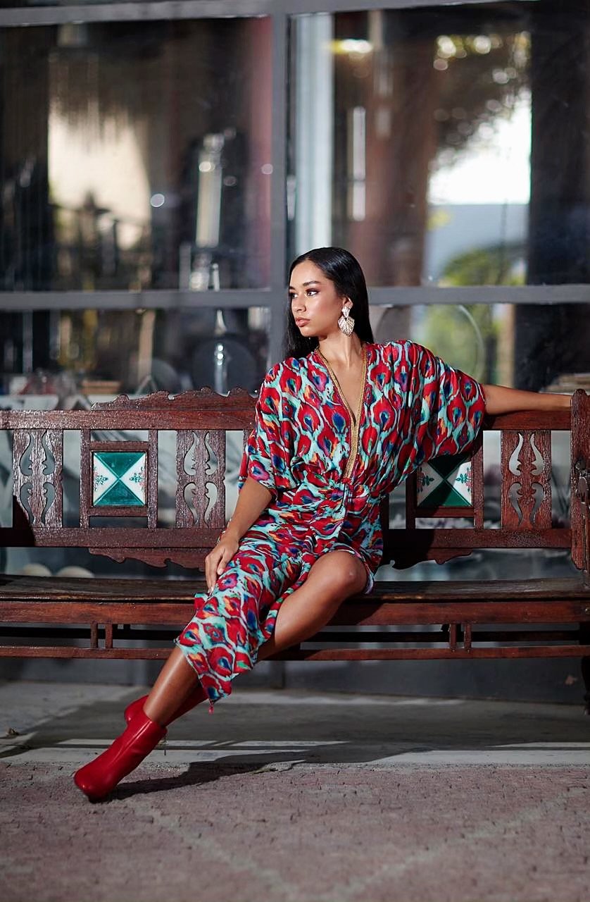 Woman in a colorful dress sitting on a wooden bench outdoors.
