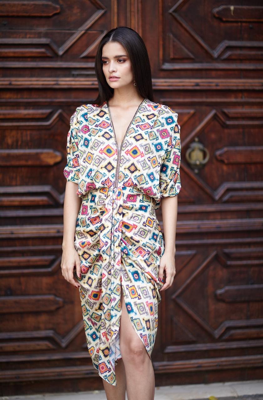 Woman wearing a colorful patterned dress standing in front of a wooden door.