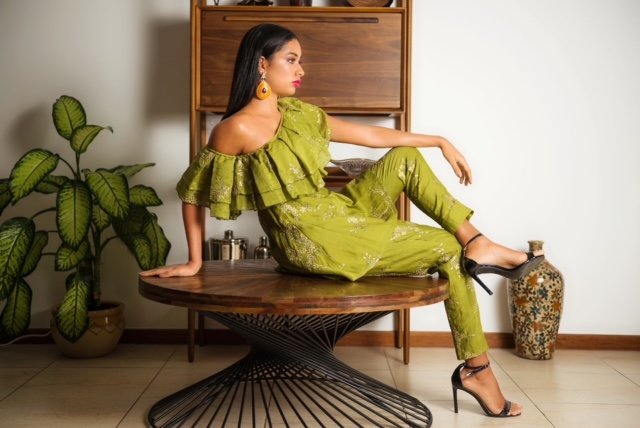 Woman in a green outfit sitting on a wooden table indoors.
