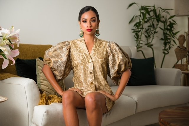 Woman in a gold patterned dress sitting on a white couch in a stylish living room.