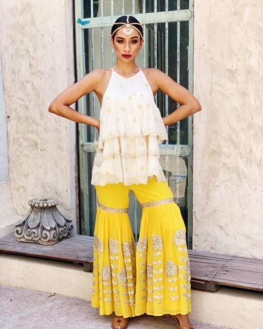 Woman wearing a white top and yellow pants with decorative patterns, standing outdoors.