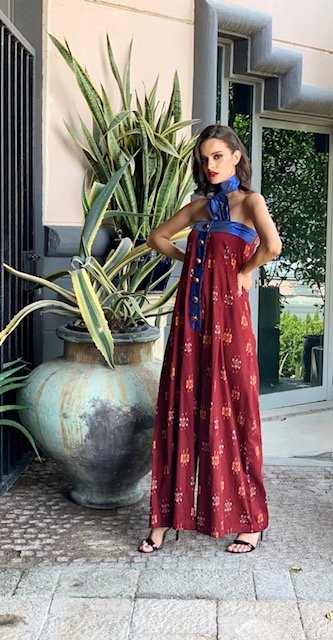 Woman in a red and blue dress standing next to a large potted plant.