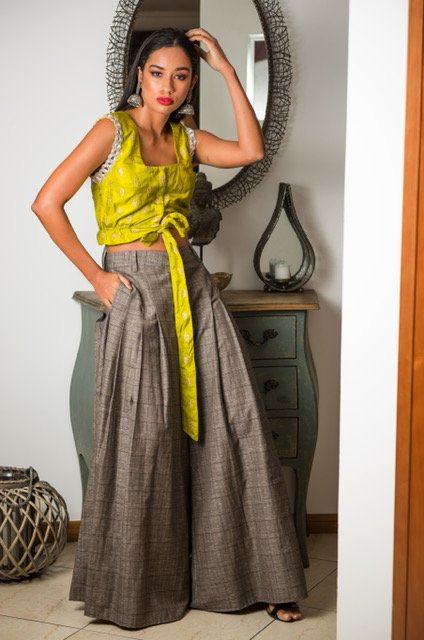 Woman wearing a yellow top and gray wide-leg pants standing in a room with a mirror and decorative items.