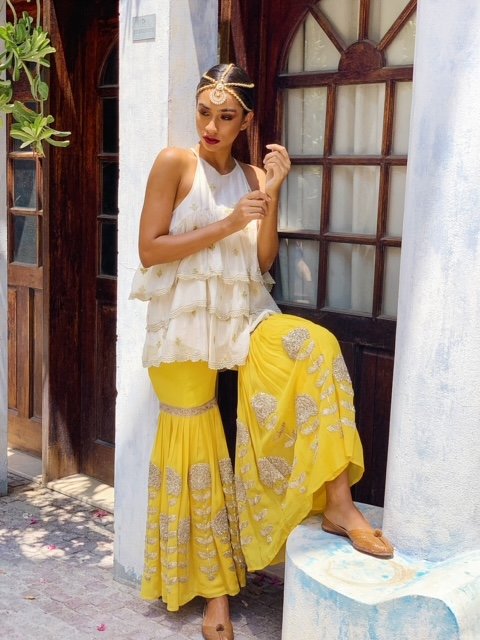 Woman in a white top and yellow skirt with patterns sitting outdoors.